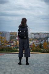 a schoolgirl with a briefcase behind her looking at the city on a cloudy autumn day