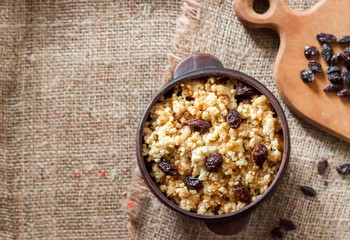 Sweet millet porridge with dark raisins in ceramic rustic bowl with walnuts in background