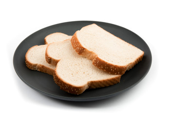 slices of a loaf of crusty white bread with sesame seeds on a black plate isolated on white