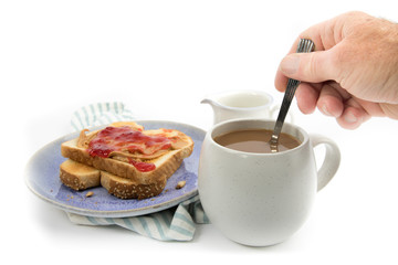 a hand stirring cream into a cup of coffee with a peanut butter and jam on toast isolated on white