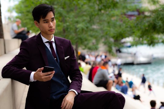 Young Businessman sitting on riverwalk holding his mobile phone, Chicago, Illinois, United States