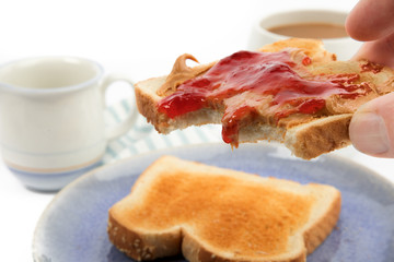a hand holding a slice of  peanut butter and jam toastwith tow bites out of it isolated on white