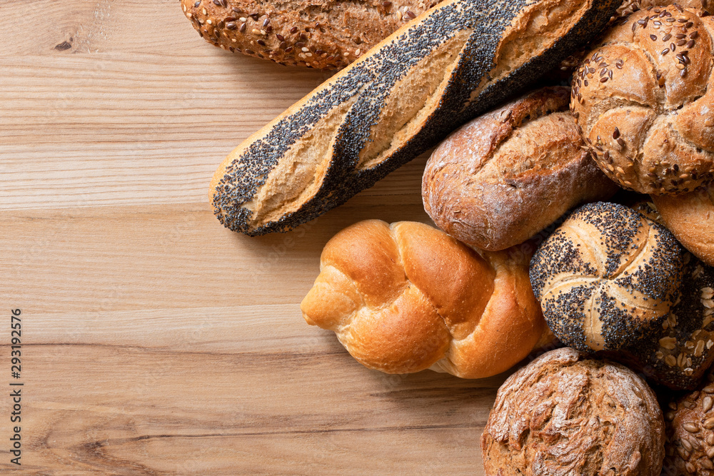 Poster Mixed baguettes and bread rolls on light wood. Top view. Space for text.