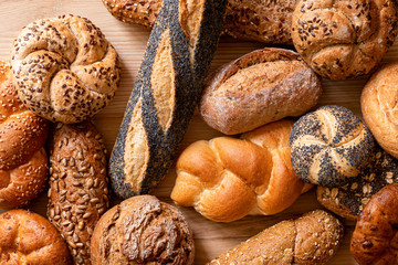 Background of mixed baguettes and bread rolls on light wood. Top view.