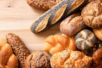 Mixed baguettes and bread rolls on light wood. Top view. Space for text.