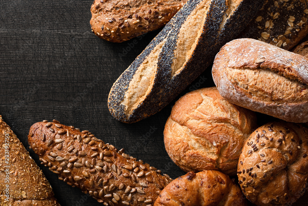 Wall mural mixed baguettes and bread rolls on dark grey wood. top view. space for text.