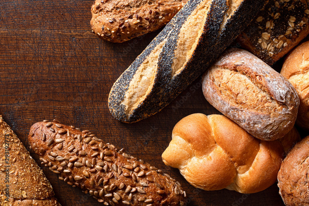 Wall mural mixed baguettes and bread rolls on rustic dark wood. top view. space for text.