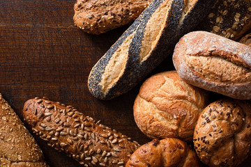 Mixed baguettes and bread rolls on rustic dark wood. Top view. Space for text.