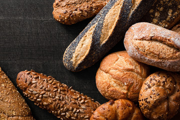Mixed baguettes and bread rolls on dark grey wood. Top view. Space for text.