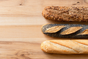 Three traditional baguettes on light wood. Plain, whole wheat and poppy seed. Top view. Space for text.