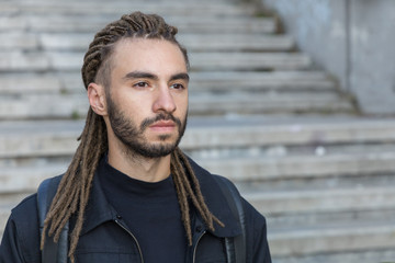 Portrait profile of a modern stylish man hairstyle with dreadlocks on the background of the stairs.
