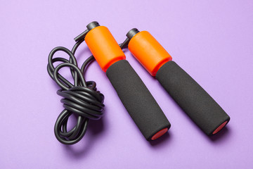 Jump rope. Fun exercises for body health. Orange rope with black cord. Violet background