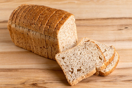 Sliced loaf of whole wheat toast bread isolated on light wood. Three slices lying.