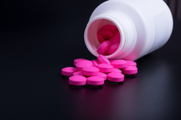 Pink pills are scattered from the jar on a black background.