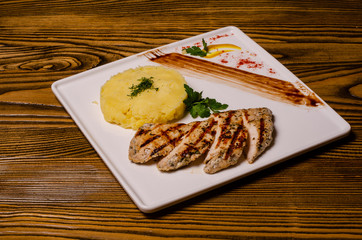 closeup two pieces of medium raw grilled meat decorated with red pepper and sauce served with potato chips and vegetable salad on black restaurant plate on wooden table.