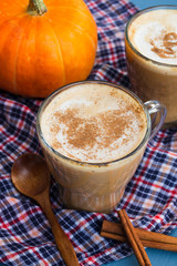 Pumpkin spiced coffee with milk and cinnamon in a glass mug. Autumn or winter hot drink on a blue wooden table. Close up
