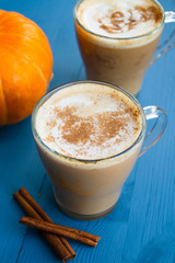 Pumpkin spiced coffee with milk and cinnamon in a glass mug. Autumn or winter hot drink on a blue wooden table. Close up