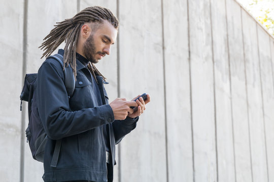 Young man with dreadlocks uses a smartphone. Read or write a message to social networks.