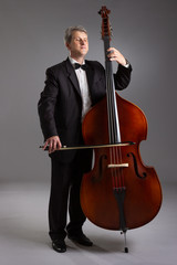 Portrait of a man with a double bass on a gray background. Musician with a big double bass.