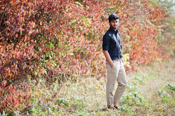 Indian man at black shirt and beige pants posed at field against autumn leaves.