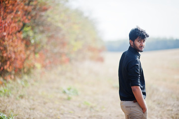 Fototapeta na wymiar Indian man at black shirt and beige pants posed at field against autumn leaves.