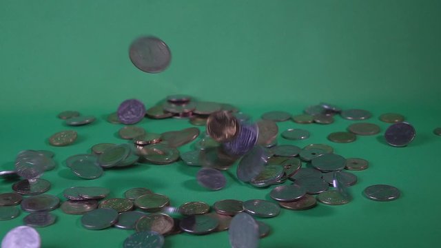 Coins of different countries fall from above on a green background, slow motion