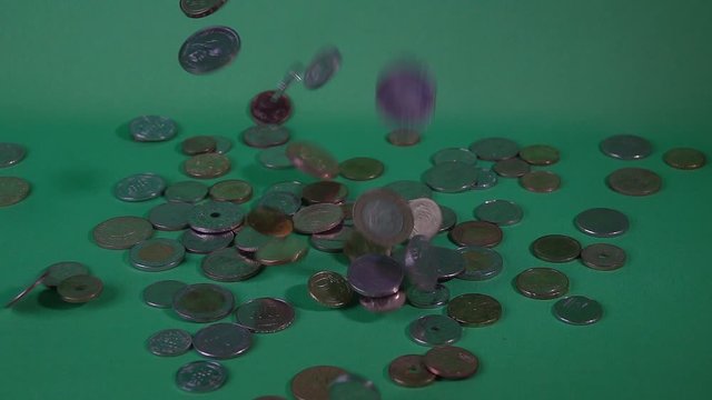 Coins of different countries fall from above on a green background, slow motion