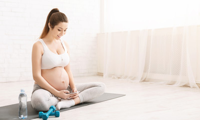 Sporty pregnant woman listening to music on her smartphone