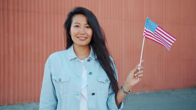 Portrait of pretty Asian girl holding official US flag outdoors smiling looking at camera expressing patriotic feelings. People, countries and tourism concept.