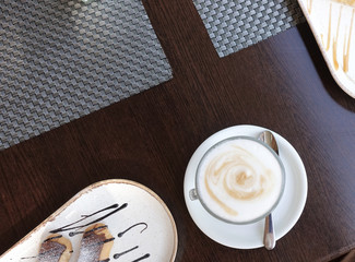 Cup of cappuccino on a served table with pastries in a cafe. View from above