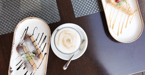 Cup of cappuccino on a served table with pastries in a cafe. View from above