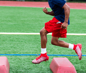 Football player running over red barriers during summer practice