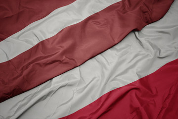 waving colorful flag of poland and national flag of latvia.