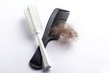 A closeup view of a hairbrush and comb, isolated against a clean white background with a clump of brunette hair, alopecia and baldness concepts. - obrazy, fototapety, plakaty
