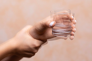 A closeup view on the hands of a person trying to hold a glass of water steady, shaking hands...