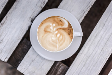 White big cup of coffee with art on white wooden table with copy space.