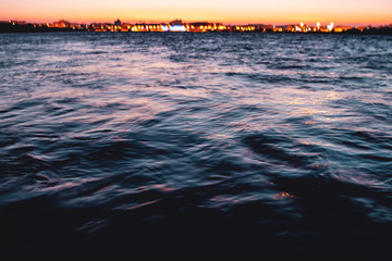 Calm evening ocean waves at the harbor marina with night life lights in the blurry background....