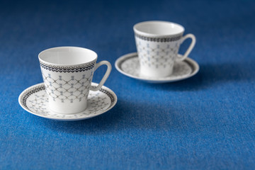 Two empty coffee cups with saucers on blue background