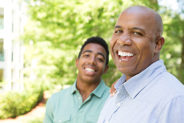 African American father and teenage son smiling.