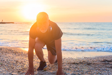 Old man start to run om sandy bach on the background of sunset sky