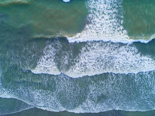 Aerial view. People enjoying their time swimming at the beach. Multiple waves gently hitting the beach.