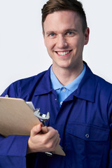 Studio Portrait Of Male Engineer With Clipboard And Spanner Against White Background