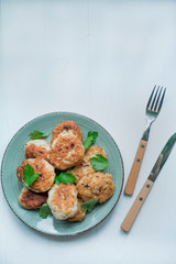 Fried meatballs with greens with a fork and knife on a light wooden background. Flat lay, close up.