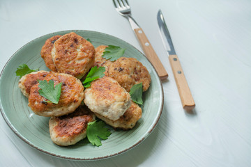 Fried meatballs with greens with a fork and knife on a light wooden background. Flat lay, close up.