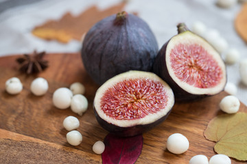 Cut fresh tasty ripe figs on desk with white snow berry, anise, fallen dry leaves, soft focus. Figs...