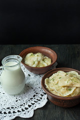 Dumplings with potatoes and cabbage. Sour cream, milk and greens. Traditional dish of Ukraine. Dark wooden background.