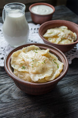 Dumplings with potatoes and cabbage. Sour cream, milk and greens. Traditional dish of Ukraine. Dark wooden background.