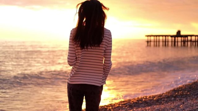 Girl shakes long hair in golden backlight of sunset. Freedom sea