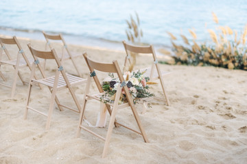 Fototapeta na wymiar Bohemian wedding bouquets on wooden chair on sand by sea ​​coast