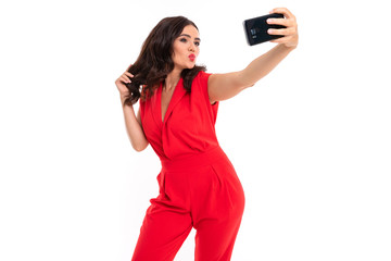 Naklejka premium brunette on a white background in a red outfit takes a selfie